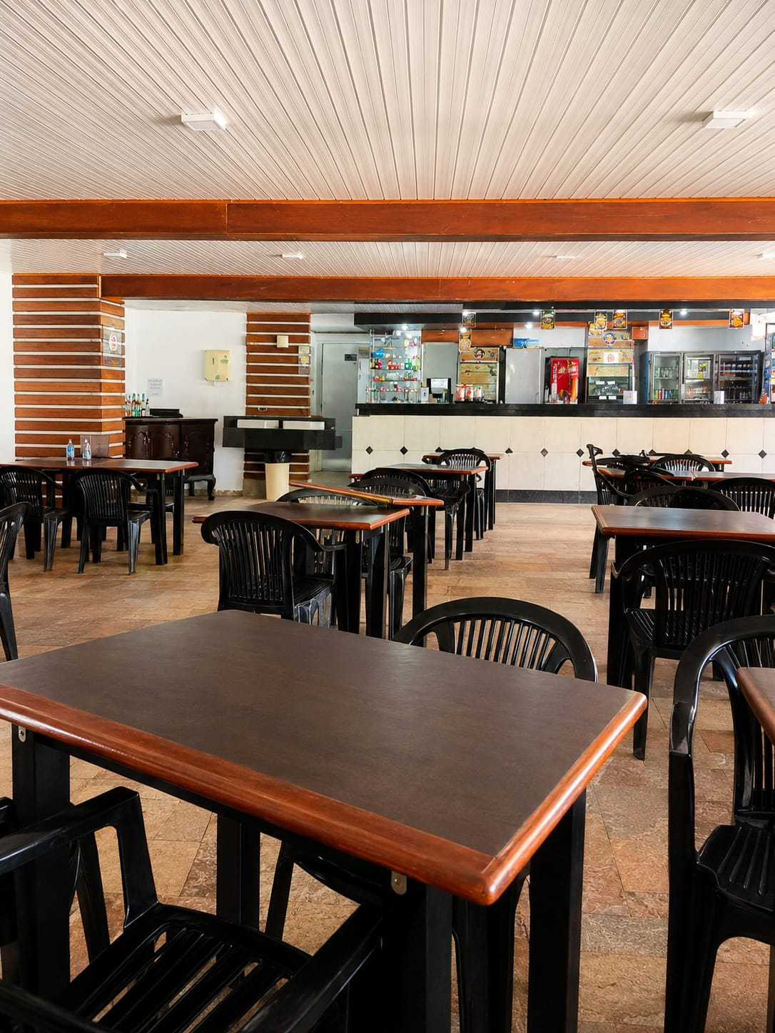 Salão do BIMA com mesas de madeira e o balcão do bar ao fundo